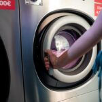 a person's hand closing the door of an industrial washing machine.