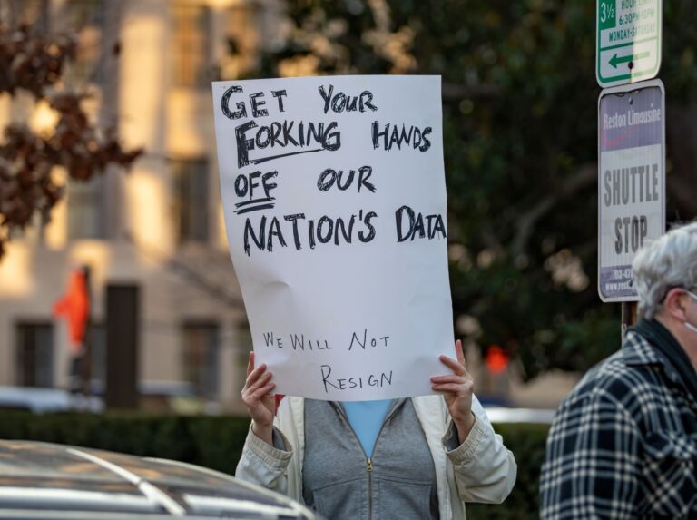 a photo of a protesters in Washington DC with a sign that says "GET YOUR FORKING HANDS OFF OUR NATION'S DATA"